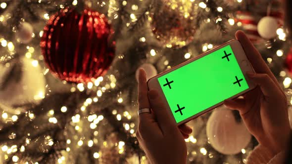Woman Is Looking at Smartphone Green Screen Near Decorated Christmas Tree.