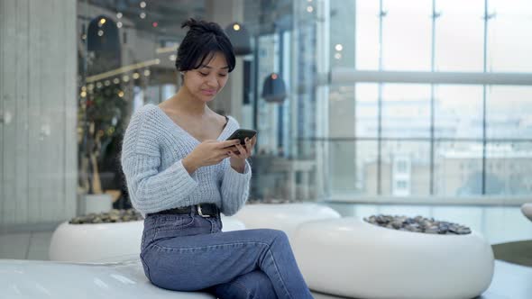 Middle Shot of Young Asian Girl Texting Sitting in Rest Zone of Shopping Mall