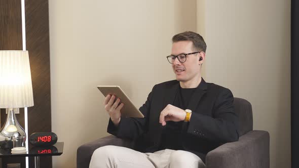 Male in Elegant Suit Sit on Couch Working on Digital Tabletwearing Wireless Headphones