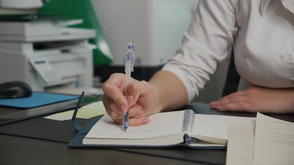 Young Female Doctor Writing Words in Cursive in Notebook with Blue Ink Pen alt