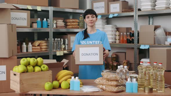 Woman Standing at Food Bank and Holding Donation Box alt