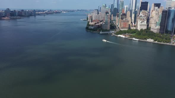 An aerial view of Upper Bay with a boat sailing by. The drone dolly in looking at lower Manhattan, t alt
