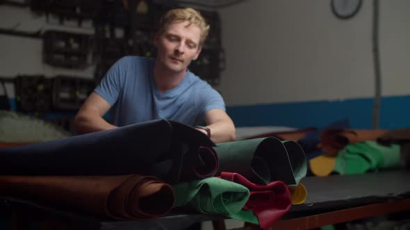 Craftsman Choosing Leather Material From Multicolored Rolls Indoors alt