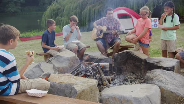 Kids at summer camp by campfire with leader playing guitar