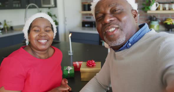 Happy african american senior couple in santa hats on video call at christmas time alt