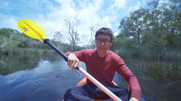 An Asian man, a tourist, paddling a boat or kayak, talking to his friends on video call conference alt