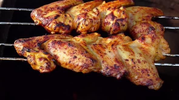 Delicious Chicken Wings on the Skewers are Frying and Rotating Above the Fire alt