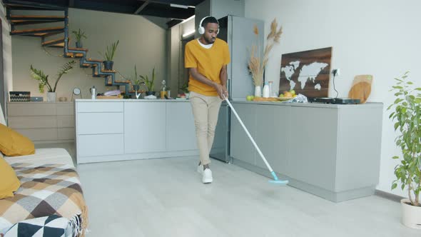 Guy Wearing Headphones Mopping Floor in Kitchen and Dancing Having Fun Doing Housework alt