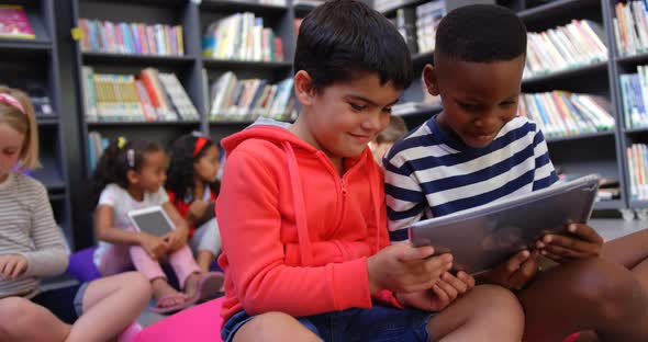 Front view of mixed-race schoolboys studying on digital tablet in the school library 4k alt