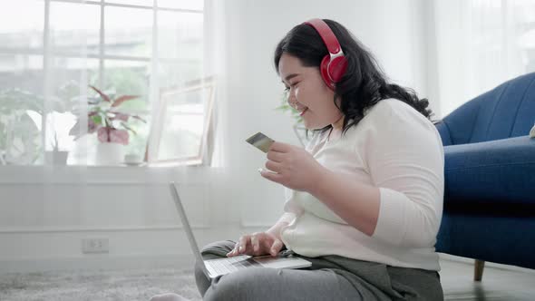 plus-size woman is happily using her online shopping credit card in her room.