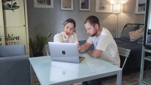 Portrait young couple sitting in front of a notebook at home. Handsome brunette man alt
