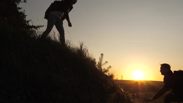 A Male Traveler Holds Out His Hand To Female Traveler Climbing a Hilltop. Tourists Climb alt