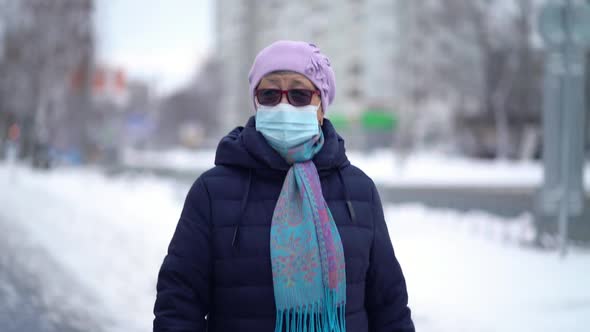 Elderly Woman in a Medical Face Mask Is Walking the Street