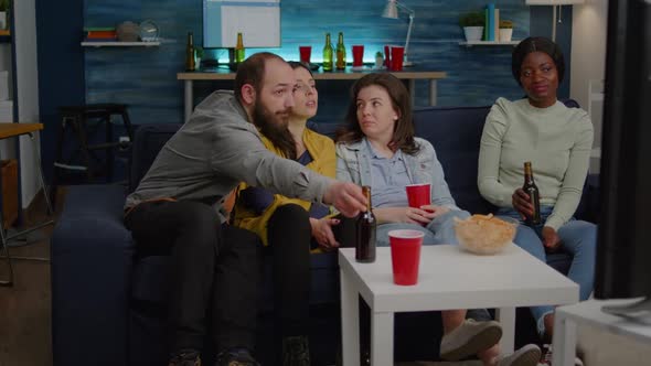 Multiracial Friends Sitting on Couch Watching Fun Movie on Television During Home Party alt