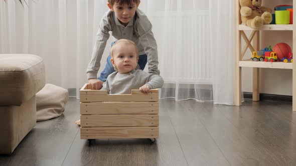 Two brothers playing and riding in wooden toy box. alt