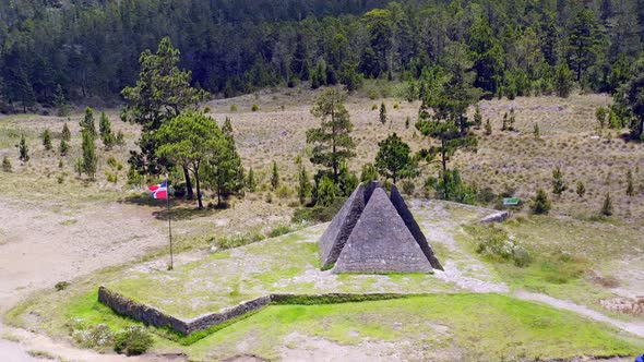 Aerial orbit shot of Colossal Pyramid, Valle Nuevo and waving flag surrounded by forest in Dominican alt