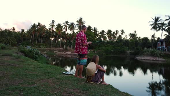 Young couple fishing near tropical lake in Vietnam, static back view alt