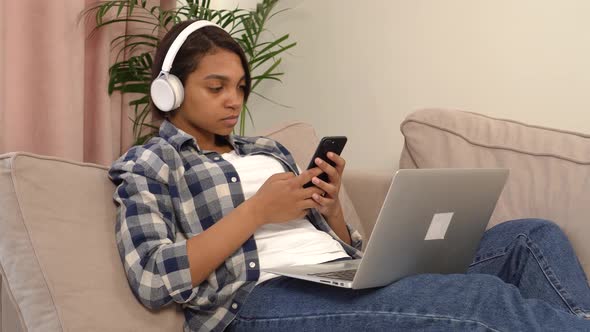 A Woman in Jeans Using a Silver Laptop and Smartphone While Lying on the Couch