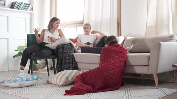 Girlfriends sit on a sofa, a chair and on the floor and they communicate with each other alt