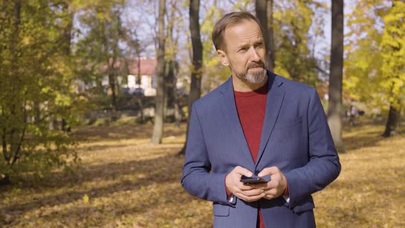 A Middleaged Handsome Caucasian Man Works on a Smartphone As He Walks Through a Park in Fall