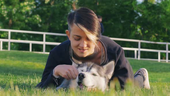 Beautiful Young Woman Playing with Funny Husky Dog Outdoors in Park alt