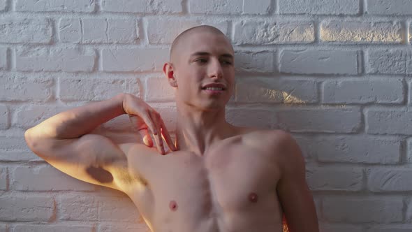 Sunrays on a Handsome Bald Shirtless Adult Gay Man in Feminine Pose in Font of White Wall alt