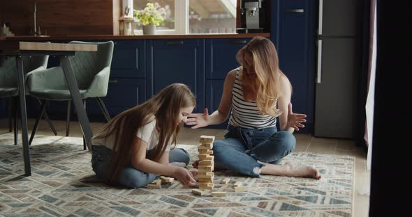 Mother and Daughter Build Tower From Wooden Bricks Sitting on a Floor at Home alt