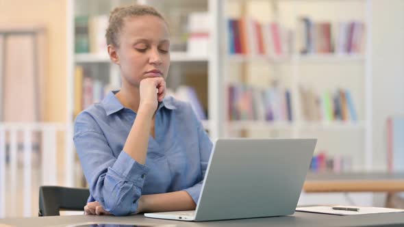 Pensive African Woman Thinking and Working on Laptop in Library alt