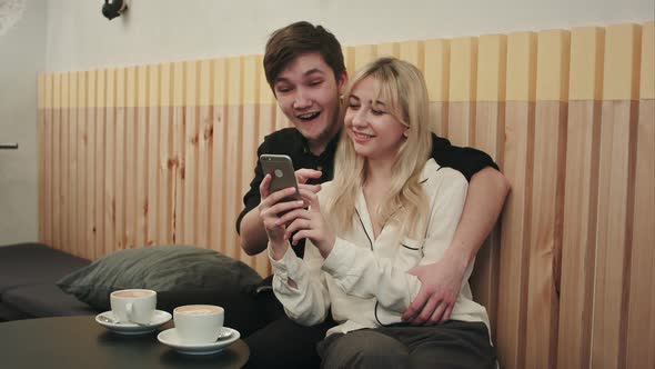 Happy Couple Using Smartphone Together and Laughing in Cafe alt