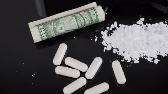 Money and drugs on a black glass table. Money, syringe and drugs. alt