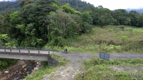A motorcyclist is driving over a small bridge and a dirtroad alt