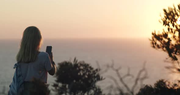 Woman Holding Phone and Makes Photo of Sunset Over the Sea Horizon alt