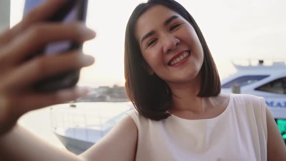 Asian woman blogger tourist with casual style use smartphone take selfie enjoy with beautiful sunset