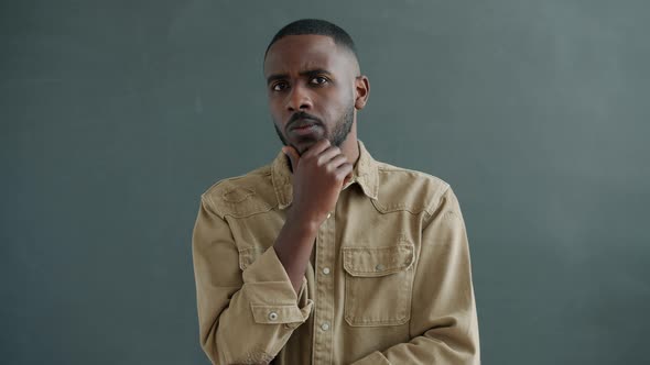 Slow Motion Portrait of Thoughtful AfroAmerican Young Man Touching Chin and Thinking alt