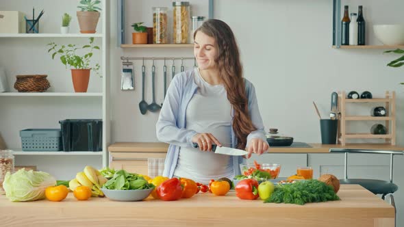 Happy Pregnant Woman Enjoying Preparing a Salad Cutting Organic Vegetables alt