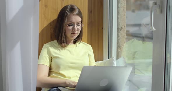 Young Beautiful Woman with Laptop is Sitting Near the Window and Chatting