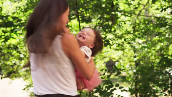 Mother Hugs Adorable Baby and Whirls with Her in Sunny Summer Park