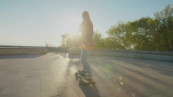Rear View of Pretty Female Skater Skateboarding at Sunrise alt