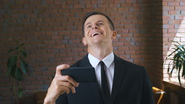 Portrait of Young Businessman Man Watching Funny Videos on a Smartphone in a Modern Office