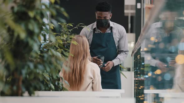 Young Professional Male Waiter in Apron Restaurant Worker in Medical Mask Serves Client in Cafe alt