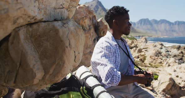 African american man hiking in countryside taking photos by the coast alt