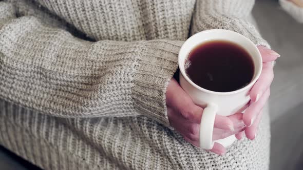 woman in a white knitted sweater holds a mug of delicious hot tea.