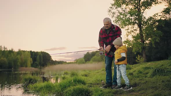 Old Fisherman is Showing to His Grandson How to Fish By Rod Grandfather and Child are Resting in alt