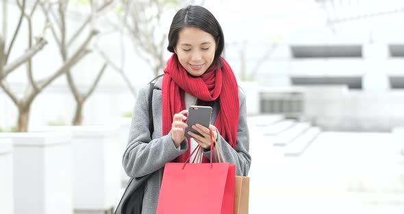 Shopping woman holding paper bag and use of mobile phone in city alt