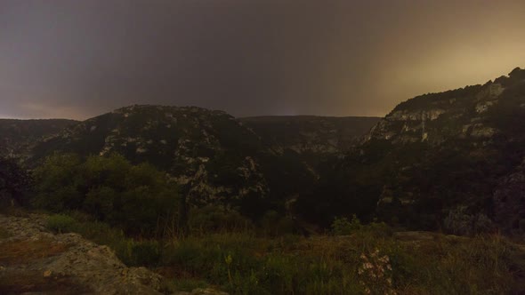 Moving clouds on night sky turning into morning dawn with golden sunrise over a canyon landscape wit