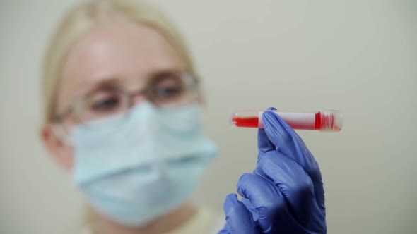 Young Woman Doctor Examines a Test Tube with Blood