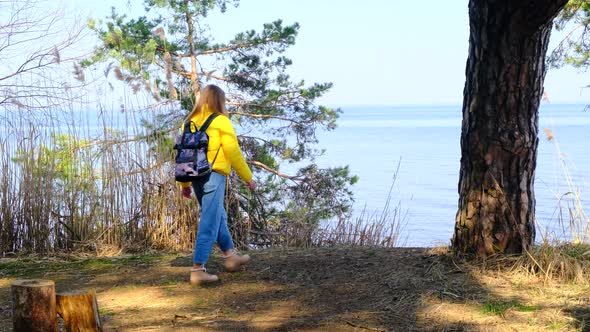 Female Tourist with Backpack is Engaged in Hiking in the Forest on the Shore of a Huge Lake or River