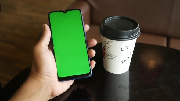 Young Man Hand Using Smart Phone with Green Screen in a Cafe alt