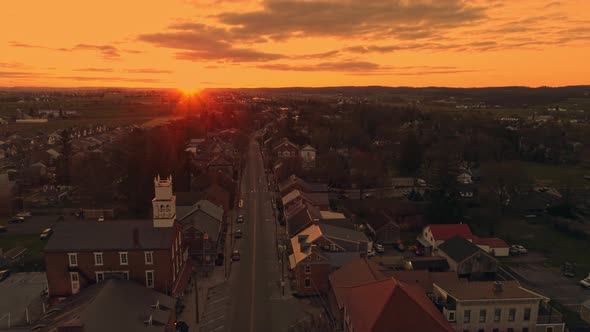Drone View of a Small Town and a Steeple as the Sunrises Behind the Camera and Breaks the Horizon alt