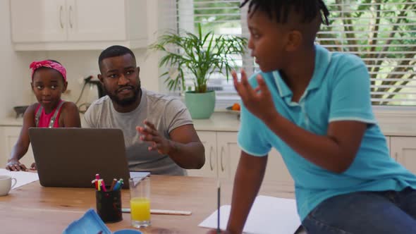 African american father using laptop and helping his son with homework at home alt